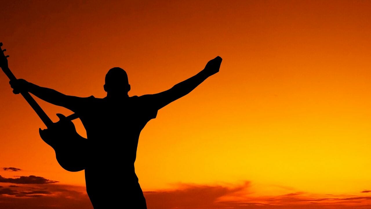 Man holding a guitar against an orange sunset