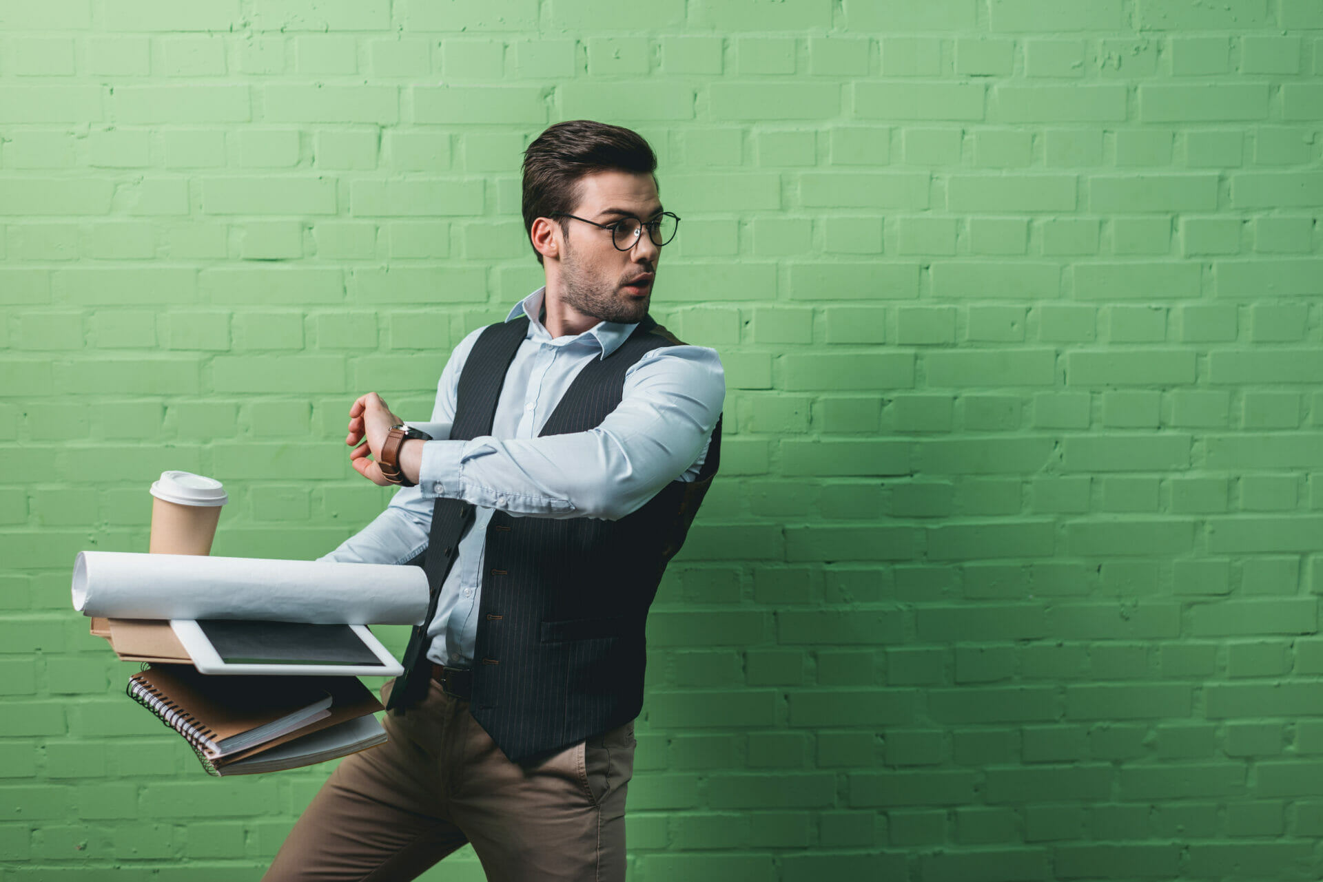 busy businessman with tablet, documents and cup of coffee in front of green wall