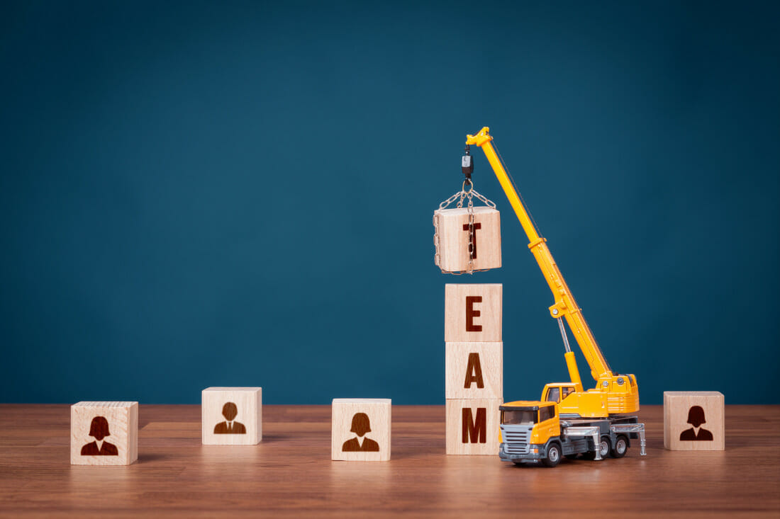 wooden blocks with images of people on one side, a toy crane is lifting blocks into a tower to spell the word team
