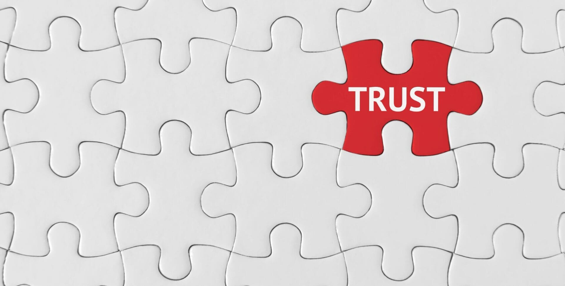 A white jigsaw with one red piece which has the word trust written on it