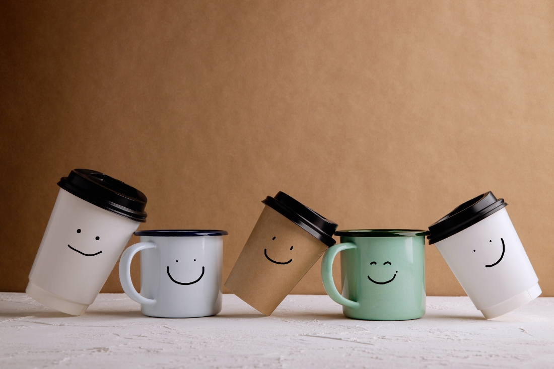 a picture of 5 disposable coffee cups each with a smiley face drawn on them representing friends at work