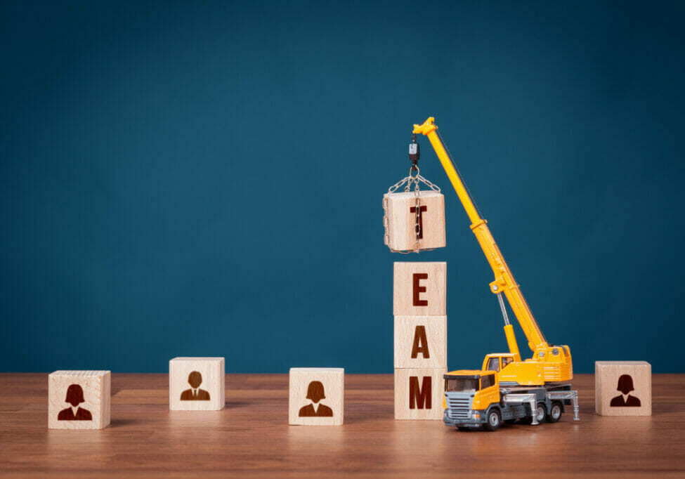 wooden blocks with images of people on one side, a toy crane is lifting blocks into a tower to spell the word team