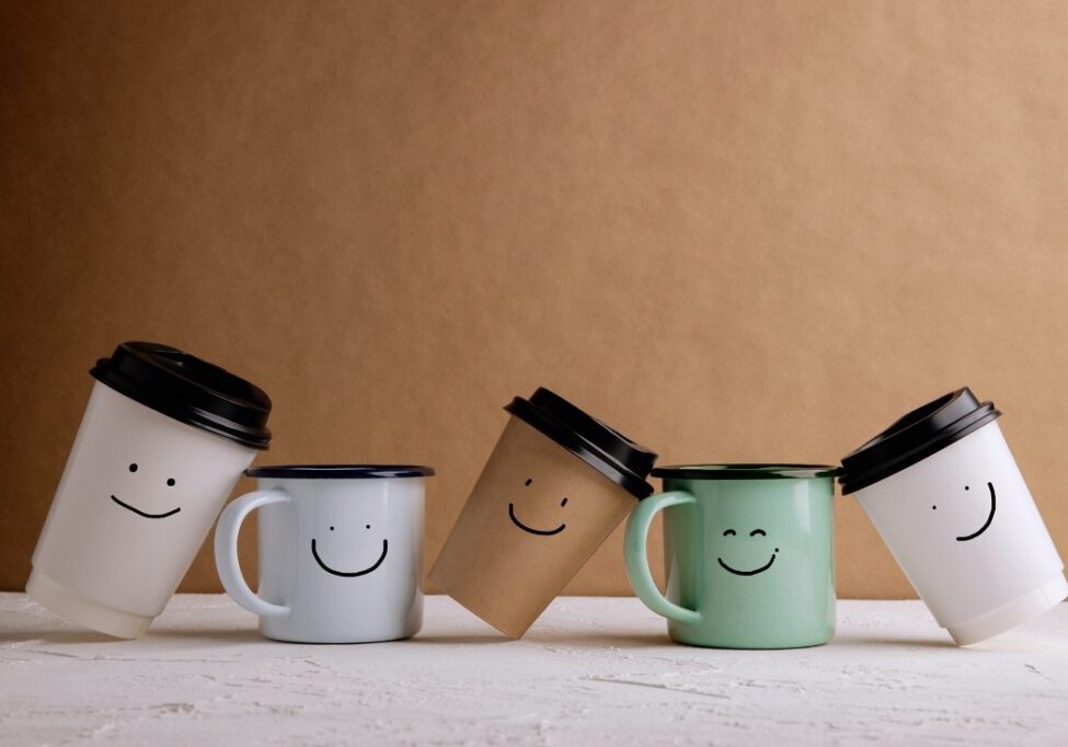 a picture of 5 disposable coffee cups each with a smiley face drawn on them representing friends at work